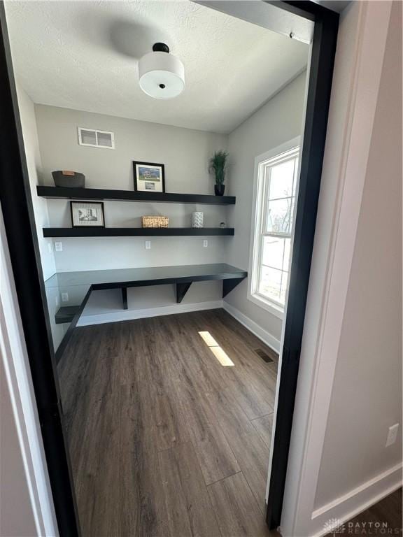 unfurnished office with visible vents, a textured ceiling, baseboards, and wood finished floors