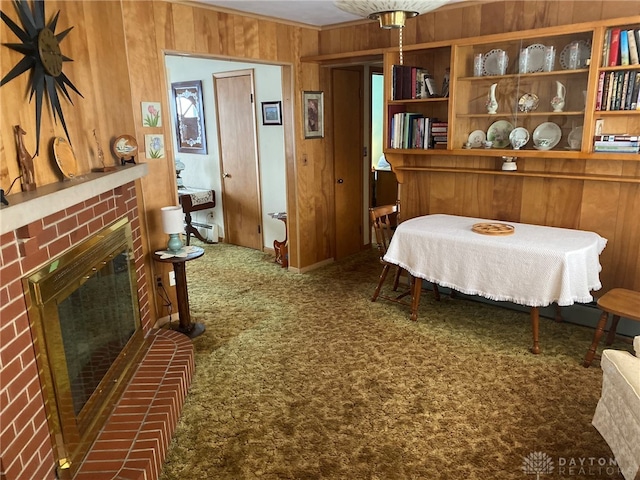 carpeted dining area featuring a brick fireplace and wooden walls