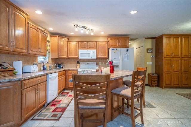 kitchen featuring a kitchen breakfast bar, backsplash, white appliances, light tile patterned floors, and a center island