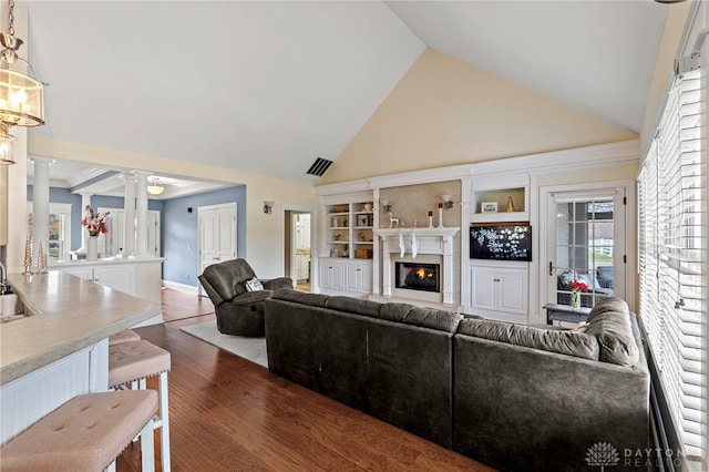 living room featuring dark hardwood / wood-style flooring, high vaulted ceiling, and ornate columns