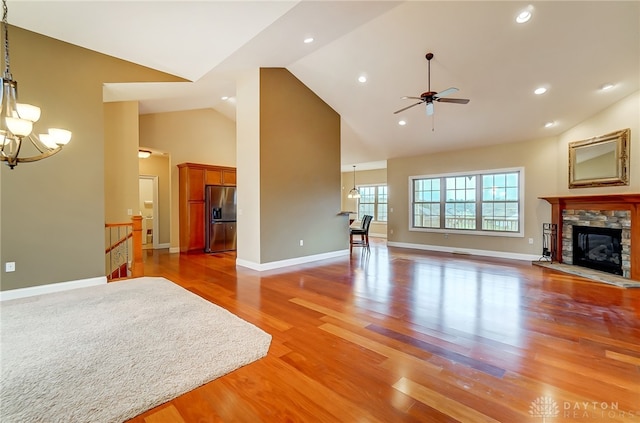 living room featuring hardwood / wood-style floors, ceiling fan with notable chandelier, high vaulted ceiling, and a stone fireplace