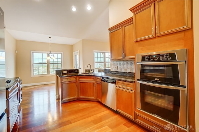 kitchen with pendant lighting, light wood-type flooring, appliances with stainless steel finishes, and dark stone counters