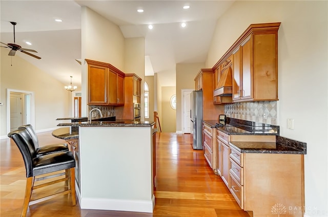 kitchen with tasteful backsplash, light hardwood / wood-style flooring, a kitchen bar, appliances with stainless steel finishes, and custom exhaust hood