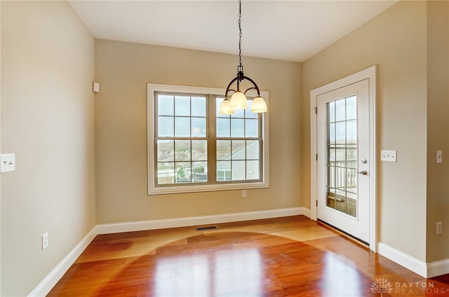 unfurnished dining area featuring a chandelier and wood-type flooring