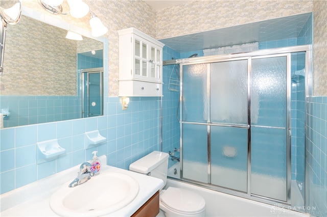 full bathroom featuring combined bath / shower with glass door, vanity, toilet, and tile walls