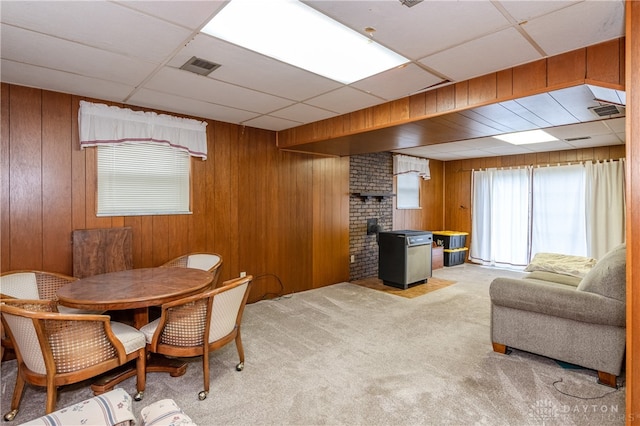 carpeted dining space with a drop ceiling and wood walls