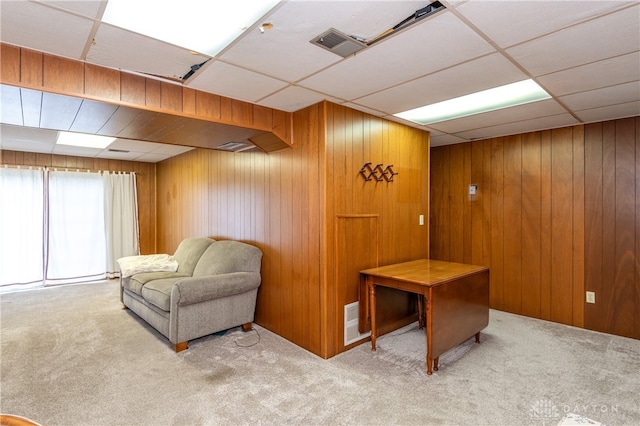 sitting room featuring a paneled ceiling, light carpet, and wood walls