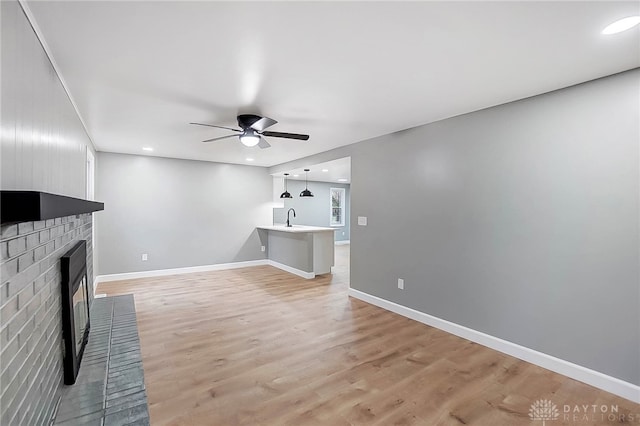 unfurnished living room featuring ceiling fan, light hardwood / wood-style floors, sink, and a brick fireplace