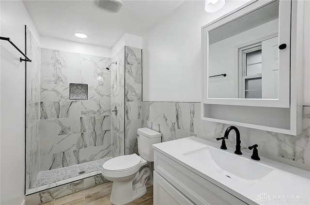 bathroom featuring a tile shower, vanity, tile walls, and toilet