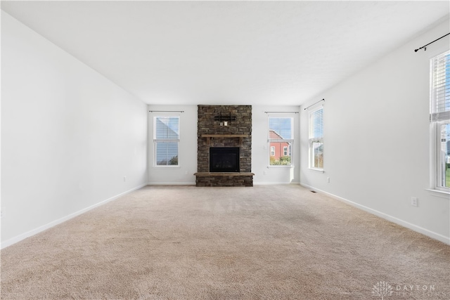 unfurnished living room with light carpet, a large fireplace, and a healthy amount of sunlight