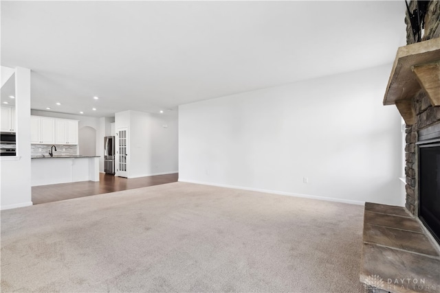 unfurnished living room featuring a stone fireplace, sink, and dark carpet