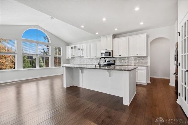 kitchen with lofted ceiling, dark wood-type flooring, white cabinets, dark stone countertops, and stainless steel appliances