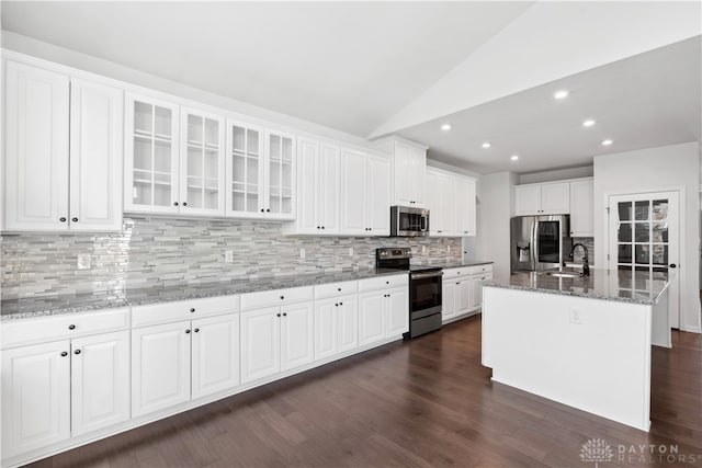 kitchen featuring stone counters, vaulted ceiling, an island with sink, appliances with stainless steel finishes, and white cabinetry