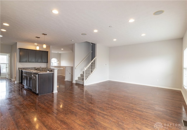 kitchen featuring sink, dark wood-type flooring, pendant lighting, a kitchen island with sink, and dark brown cabinets