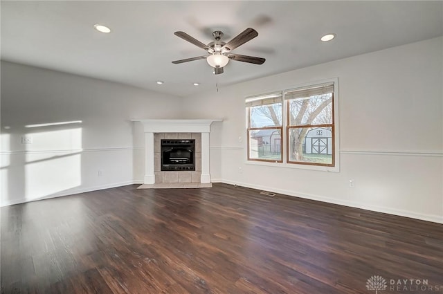 unfurnished living room with a tiled fireplace, dark wood-type flooring, and ceiling fan