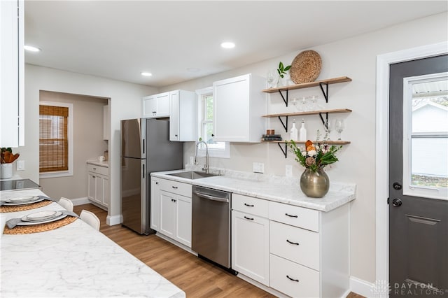 kitchen featuring appliances with stainless steel finishes, light stone counters, sink, light hardwood / wood-style flooring, and white cabinetry