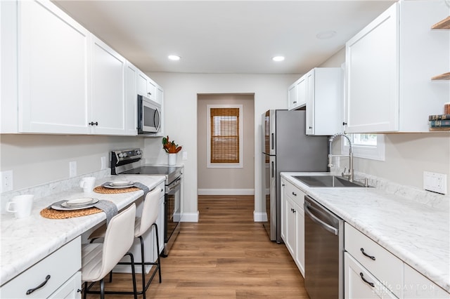 kitchen featuring light stone countertops, stainless steel appliances, sink, white cabinets, and light hardwood / wood-style floors