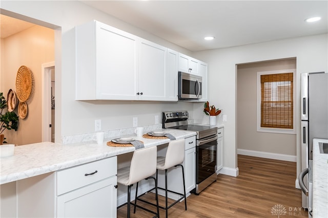 kitchen featuring light stone countertops, wood-type flooring, a kitchen bar, white cabinets, and appliances with stainless steel finishes