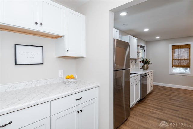 kitchen with hardwood / wood-style flooring, light stone countertops, white cabinetry, and stainless steel appliances