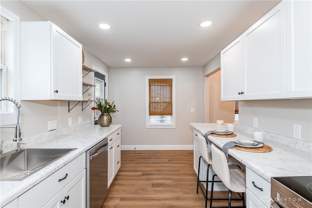 kitchen with light wood-type flooring, light stone counters, stainless steel dishwasher, sink, and white cabinets