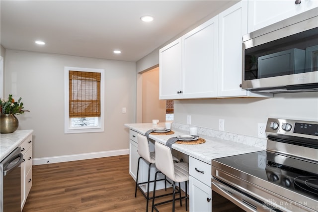 kitchen featuring stainless steel appliances, white cabinetry, dark wood-type flooring, and a breakfast bar area