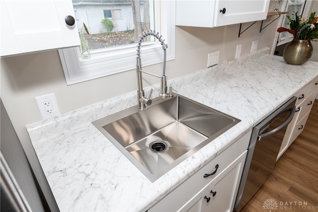 kitchen featuring light stone counters, stainless steel dishwasher, sink, wood-type flooring, and white cabinetry