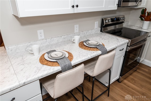 kitchen with hardwood / wood-style flooring, a kitchen bar, white cabinetry, and stainless steel appliances