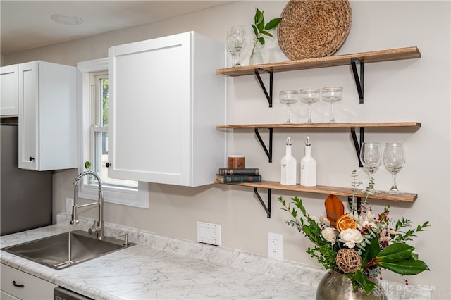 kitchen featuring light stone counters, sink, and white cabinets