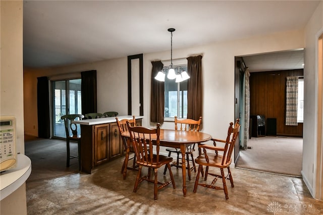 dining area with wooden walls, plenty of natural light, carpet floors, and a notable chandelier