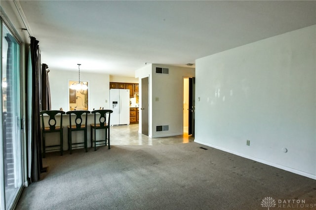 unfurnished living room featuring a notable chandelier, a healthy amount of sunlight, and light colored carpet