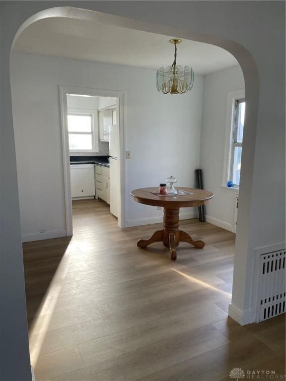 dining room featuring radiator heating unit, light hardwood / wood-style floors, and a notable chandelier