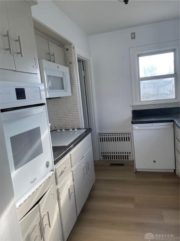 kitchen with white cabinetry, white appliances, radiator heating unit, and light hardwood / wood-style flooring