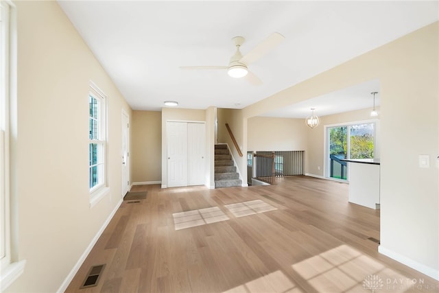 unfurnished living room with ceiling fan with notable chandelier and light wood-type flooring