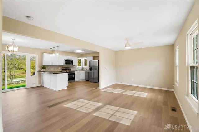 kitchen with light wood-type flooring, tasteful backsplash, stainless steel appliances, white cabinets, and hanging light fixtures