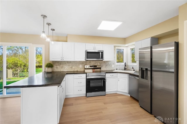 kitchen with white cabinets, sink, decorative light fixtures, kitchen peninsula, and stainless steel appliances