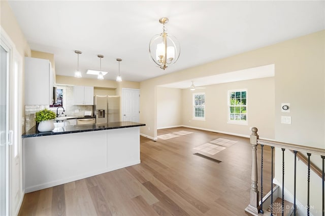 kitchen featuring appliances with stainless steel finishes, backsplash, decorative light fixtures, white cabinets, and light hardwood / wood-style floors