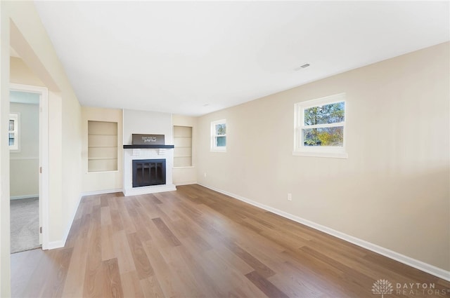 unfurnished living room featuring built in features, light hardwood / wood-style floors, and a brick fireplace