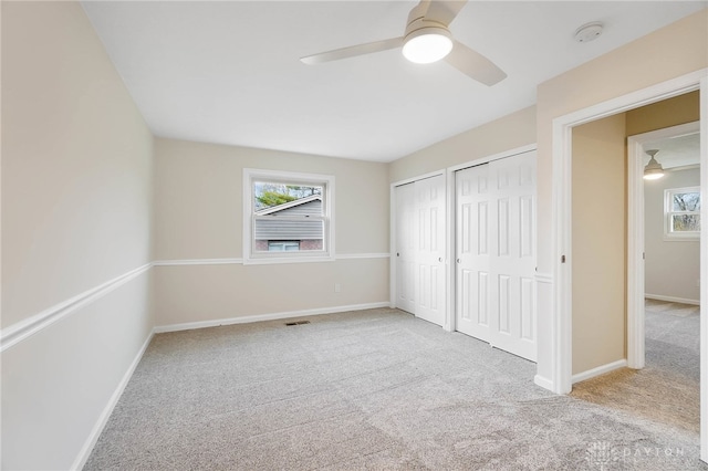 unfurnished bedroom with ceiling fan, light carpet, and two closets