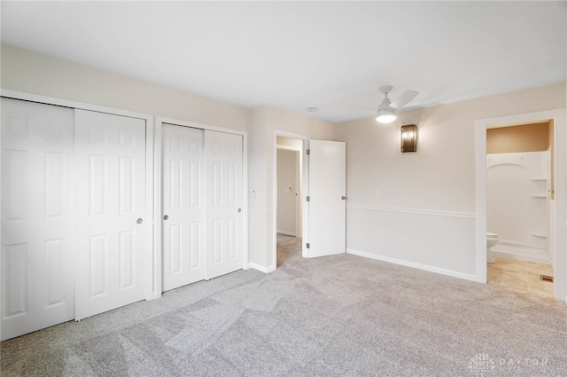 unfurnished bedroom with ensuite bath, light carpet, ceiling fan, and multiple closets