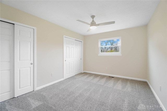 unfurnished bedroom featuring carpet flooring, ceiling fan, and multiple closets