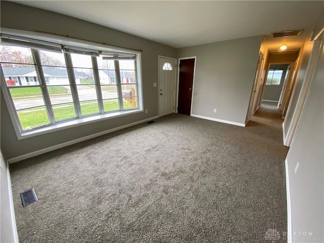 unfurnished room with a wealth of natural light and dark colored carpet