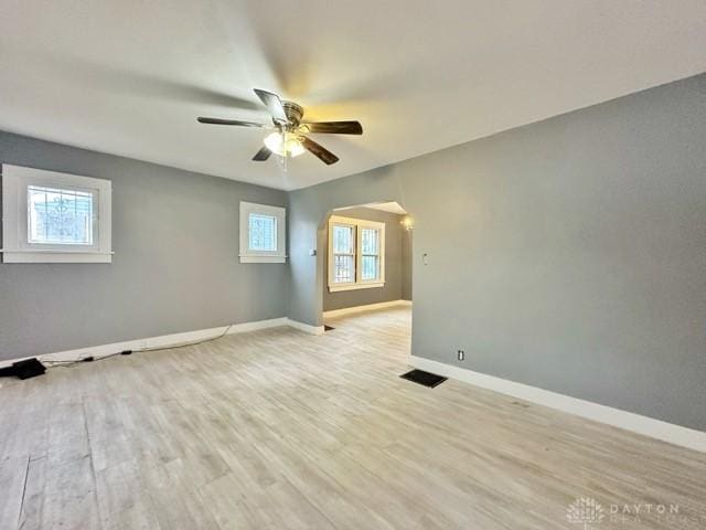 unfurnished room featuring light wood-type flooring, a healthy amount of sunlight, arched walkways, and baseboards