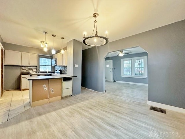 kitchen featuring arched walkways, stainless steel microwave, open floor plan, a peninsula, and backsplash