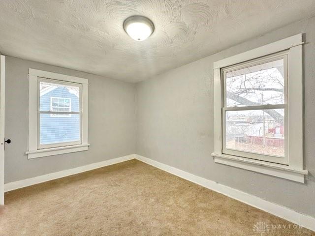 unfurnished room featuring a textured ceiling, carpet flooring, and baseboards