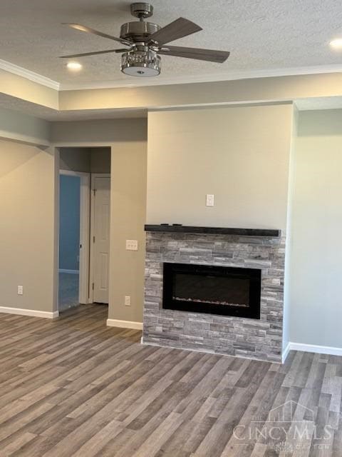 unfurnished living room with ceiling fan, a stone fireplace, hardwood / wood-style floors, a textured ceiling, and ornamental molding