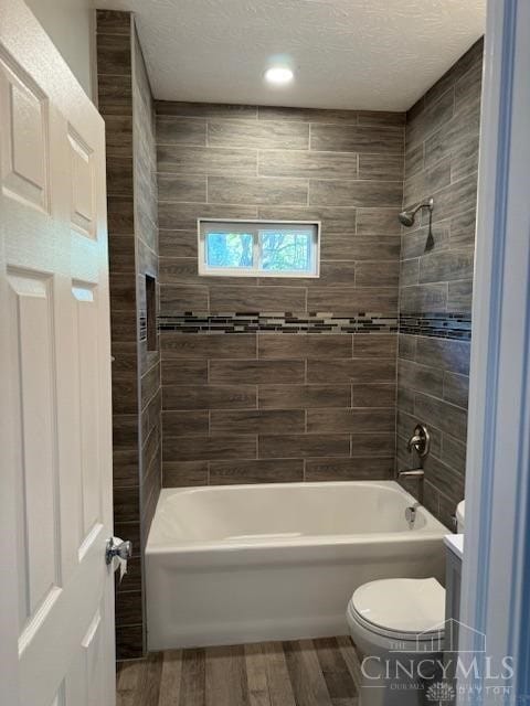 bathroom featuring hardwood / wood-style floors, toilet, tiled shower / bath, and a textured ceiling