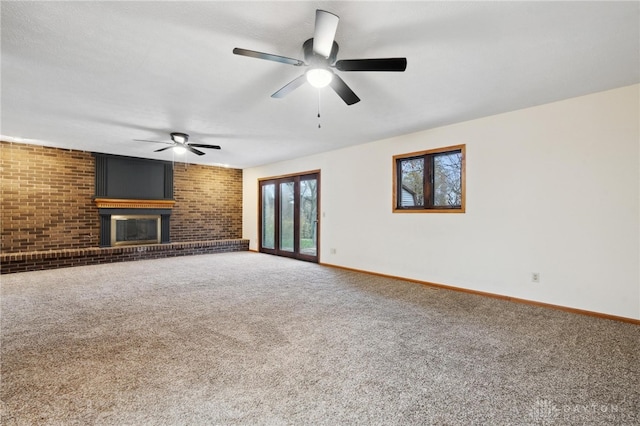 unfurnished living room featuring carpet, ceiling fan, a fireplace, and brick wall