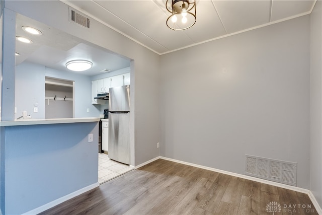 kitchen featuring white cabinetry, light hardwood / wood-style flooring, kitchen peninsula, stainless steel fridge, and crown molding