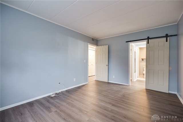 spare room with a barn door, wood-type flooring, and ornamental molding