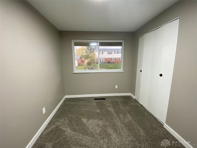 unfurnished bedroom with dark colored carpet and a closet